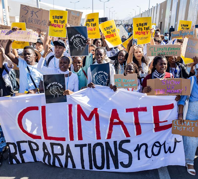 People marching holding placards and a banner reading 'Climate reparations now'