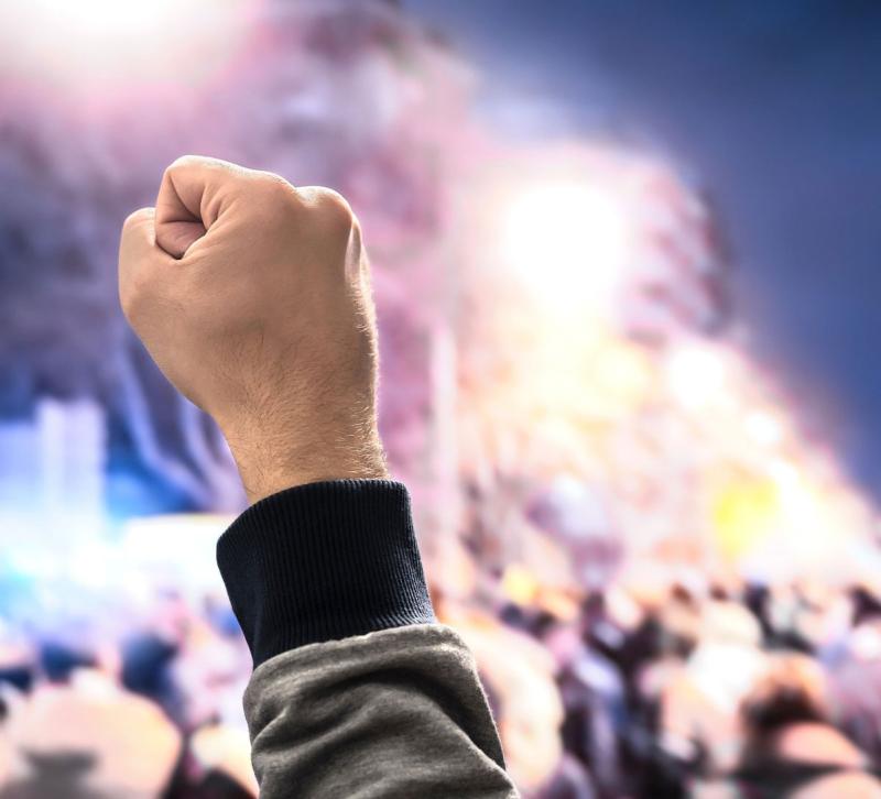 Raised fist foregrounded against protesting crowd