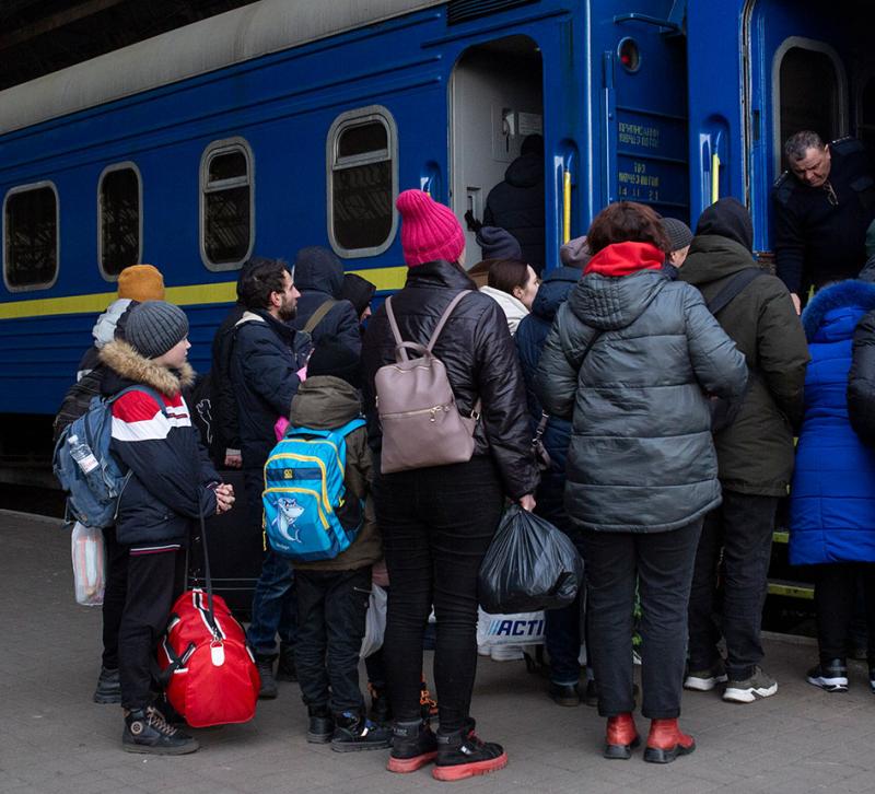 A group of people waiting to board a train bearing the blue and yellow colours of Ukraine