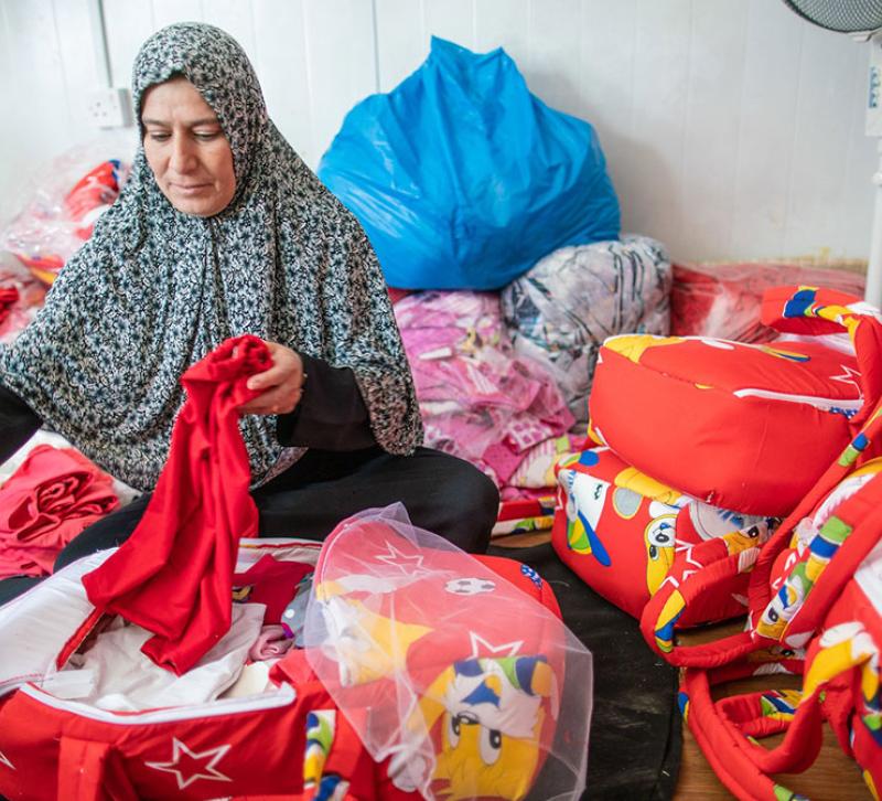 A woman surrounded by brightly coloured bags sorts through clothing