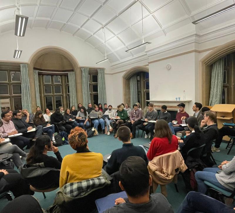 A large group of people sitting in a circle in a seminar room