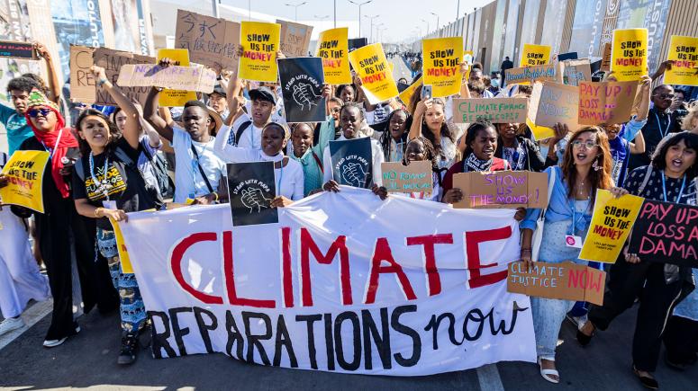 People marching holding placards and a banner reading 'Climate reparations now'