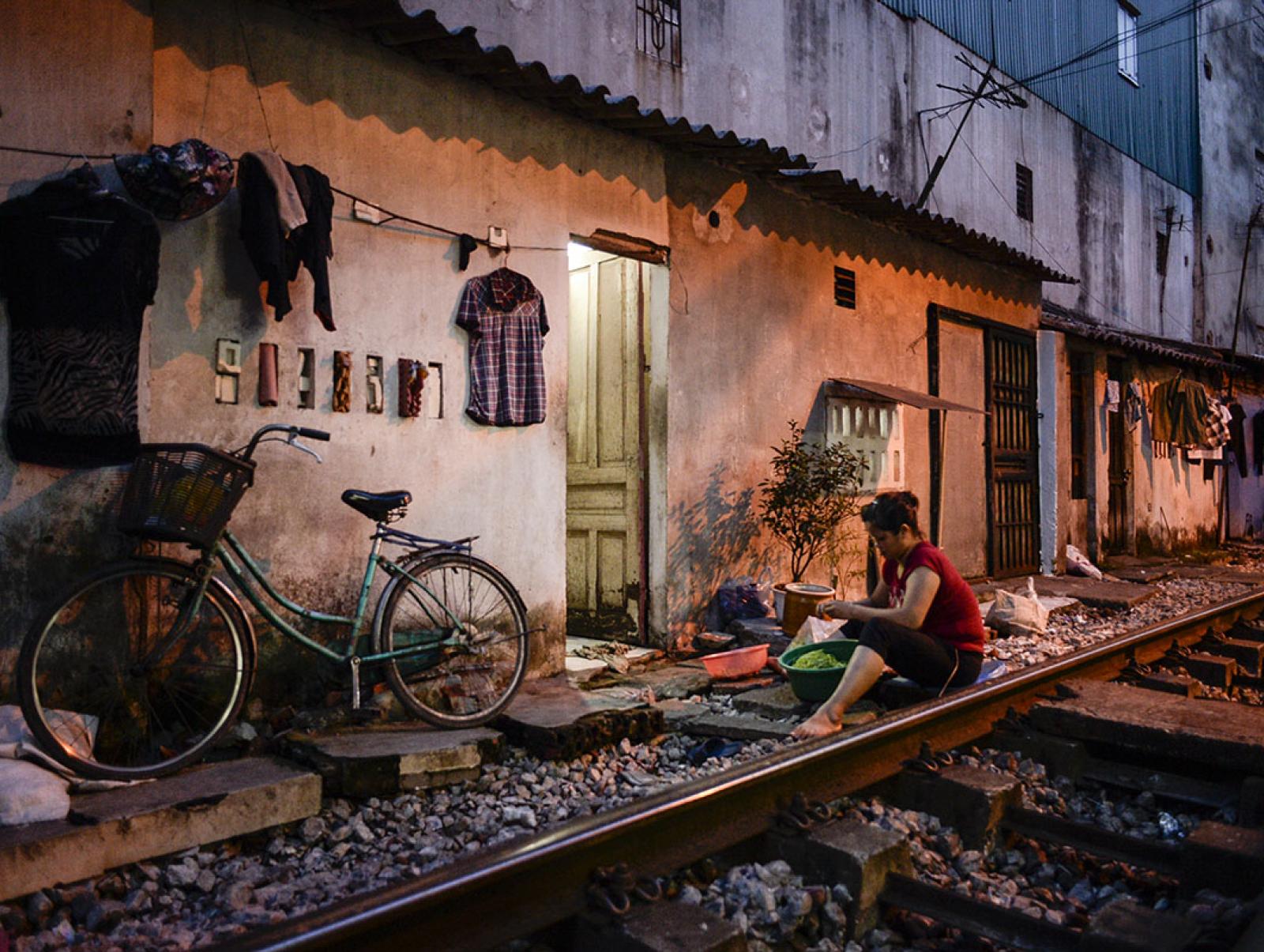 A woman seated outsidet a building with corrugated iron roof in evening light