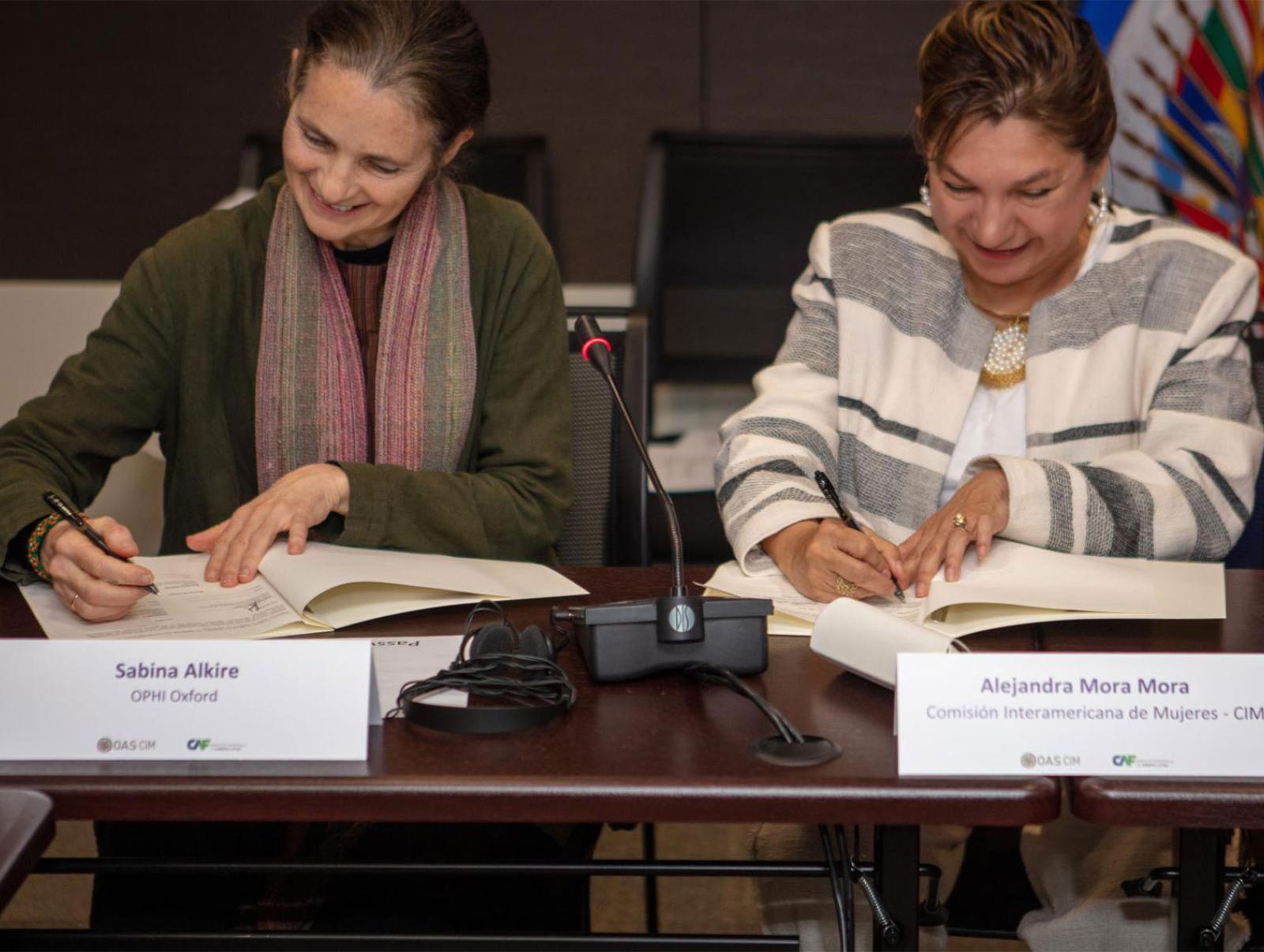 Sabina Alkire and Alejandra Mora Mora seated at a desk signing agreements