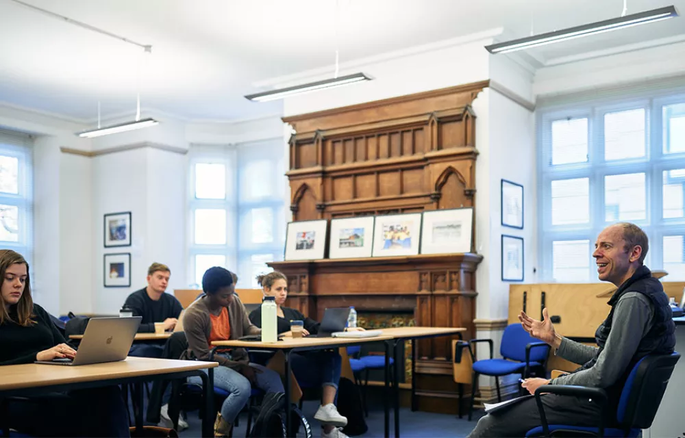 Four students sitting at tables with a professor seated at the front