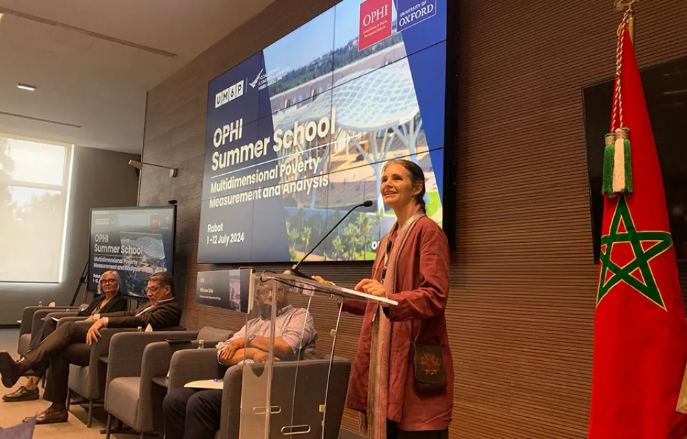 Sabina Alkire standing at a podium in front of a powerpoint display