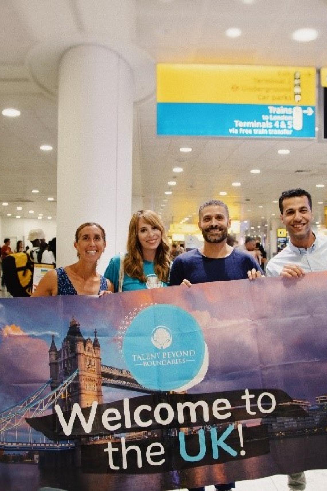 Four people at an airport holding a banner reading 'Welcome to the UK'