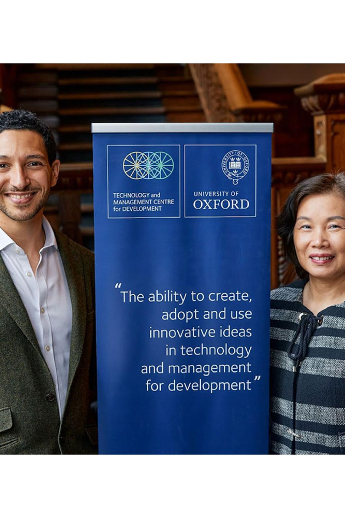 Amir Lebdioui and Xiaolan Fu standing either side of a blue banner