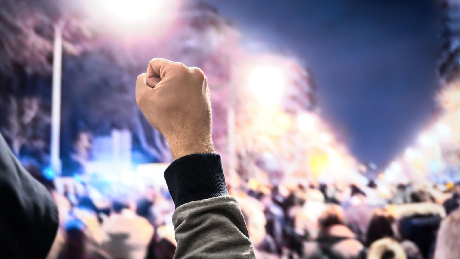 Raised fist foregrounded against protesting crowd