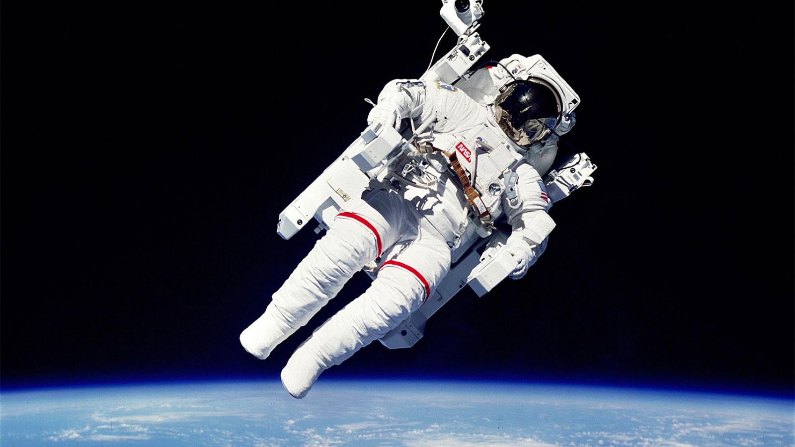 An astronaut in full space suit floating in space with the earth below