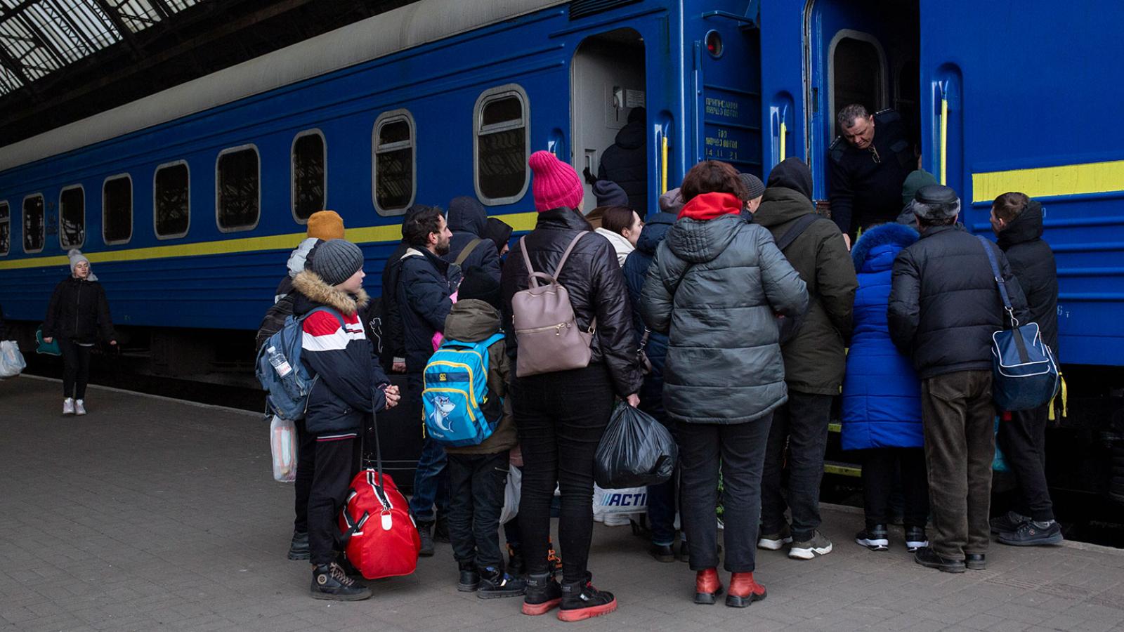 A group of people waiting to board a train bearing the blue and yellow colours of Ukraine