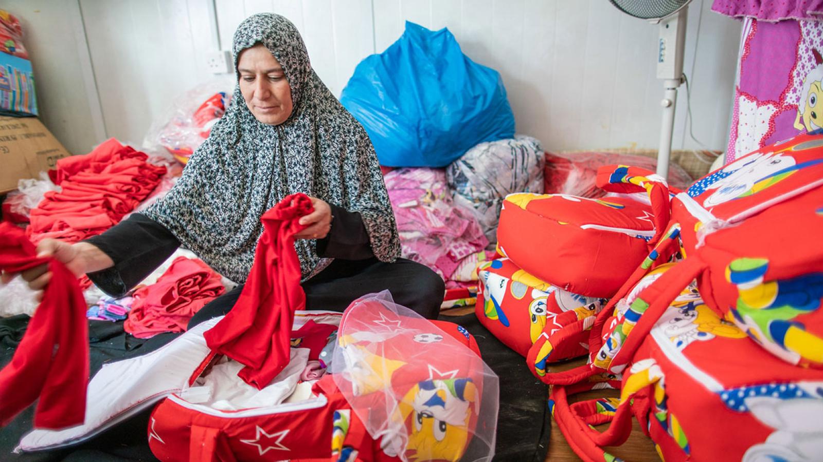 A woman surrounded by brightly coloured bags sorts through clothing