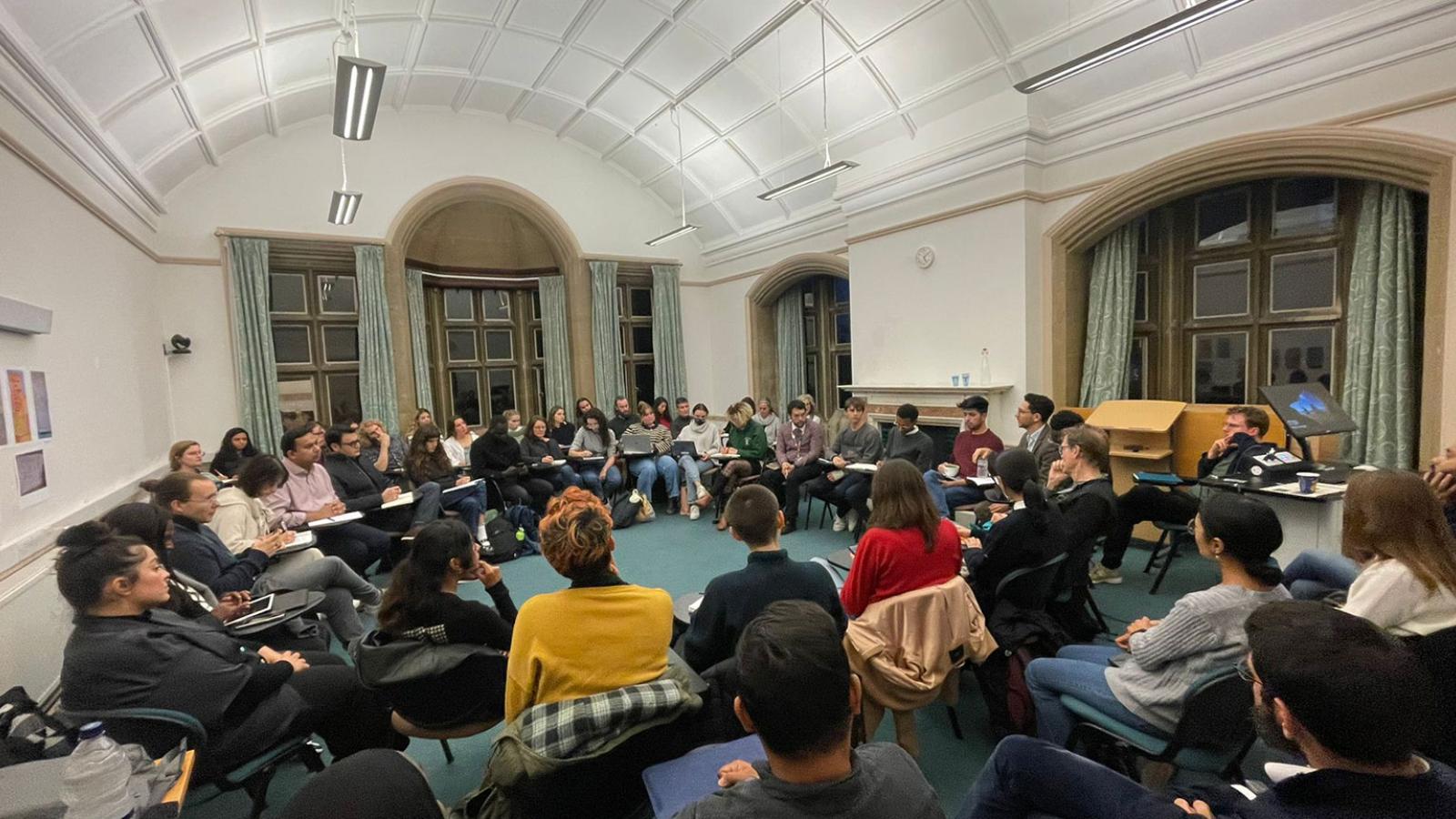 A large group of people sitting in a circle in a seminar room