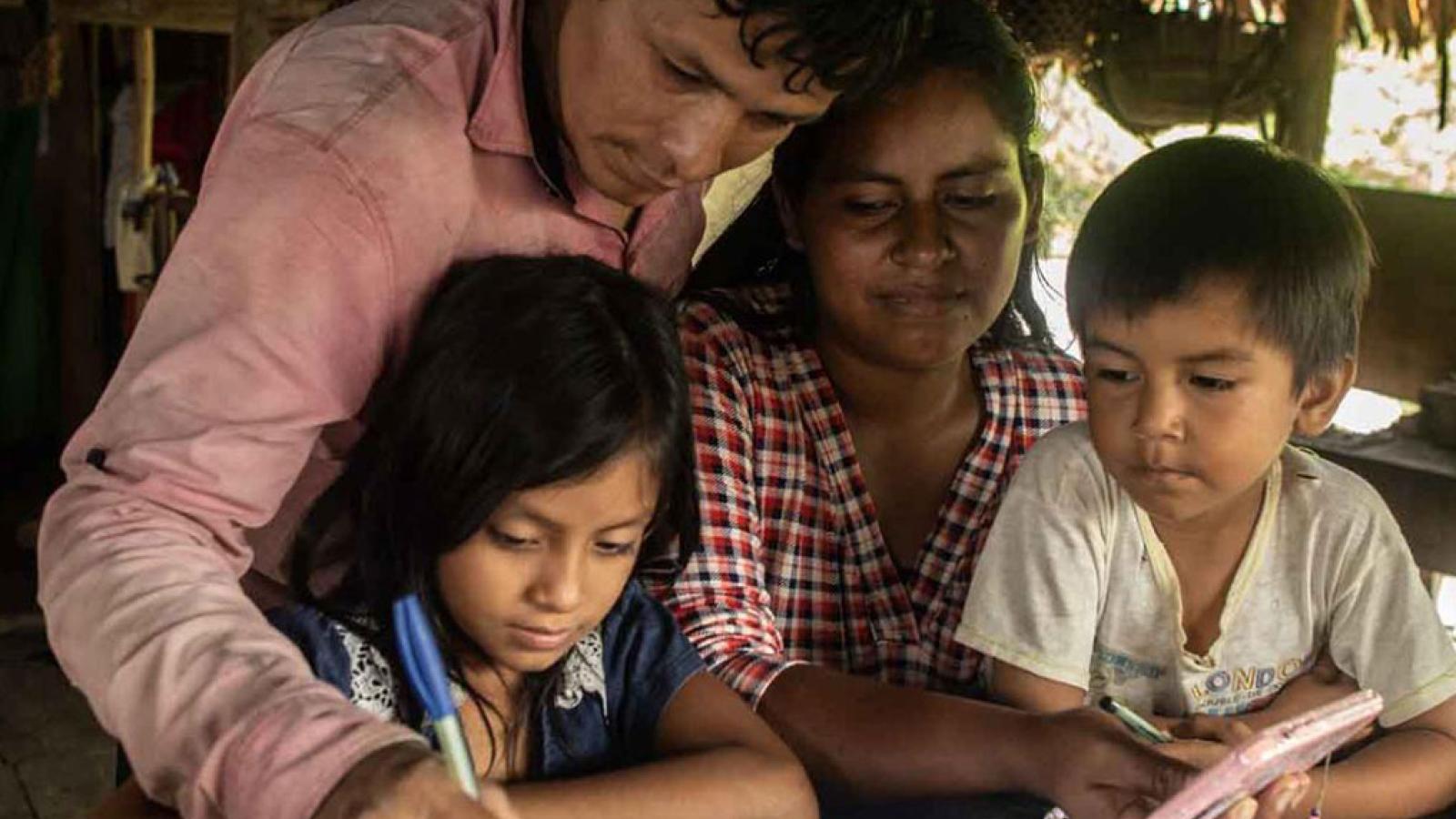 A mother and father a child write in a book while another child looks on