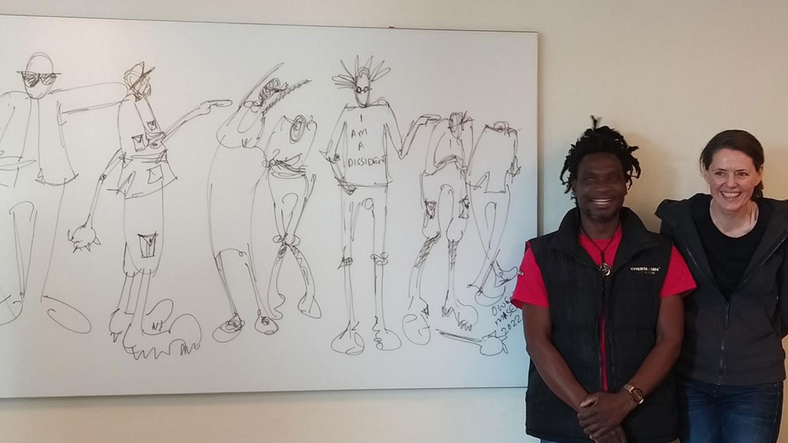Two people stand alongside a black and white illustration on the wall